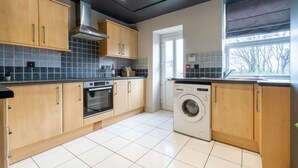 A modern kitchen with wooden cabinets, a built-in oven, a washing machine, and a window with a view. - Crookesmoor View, Sheffield (South Yorkshire)