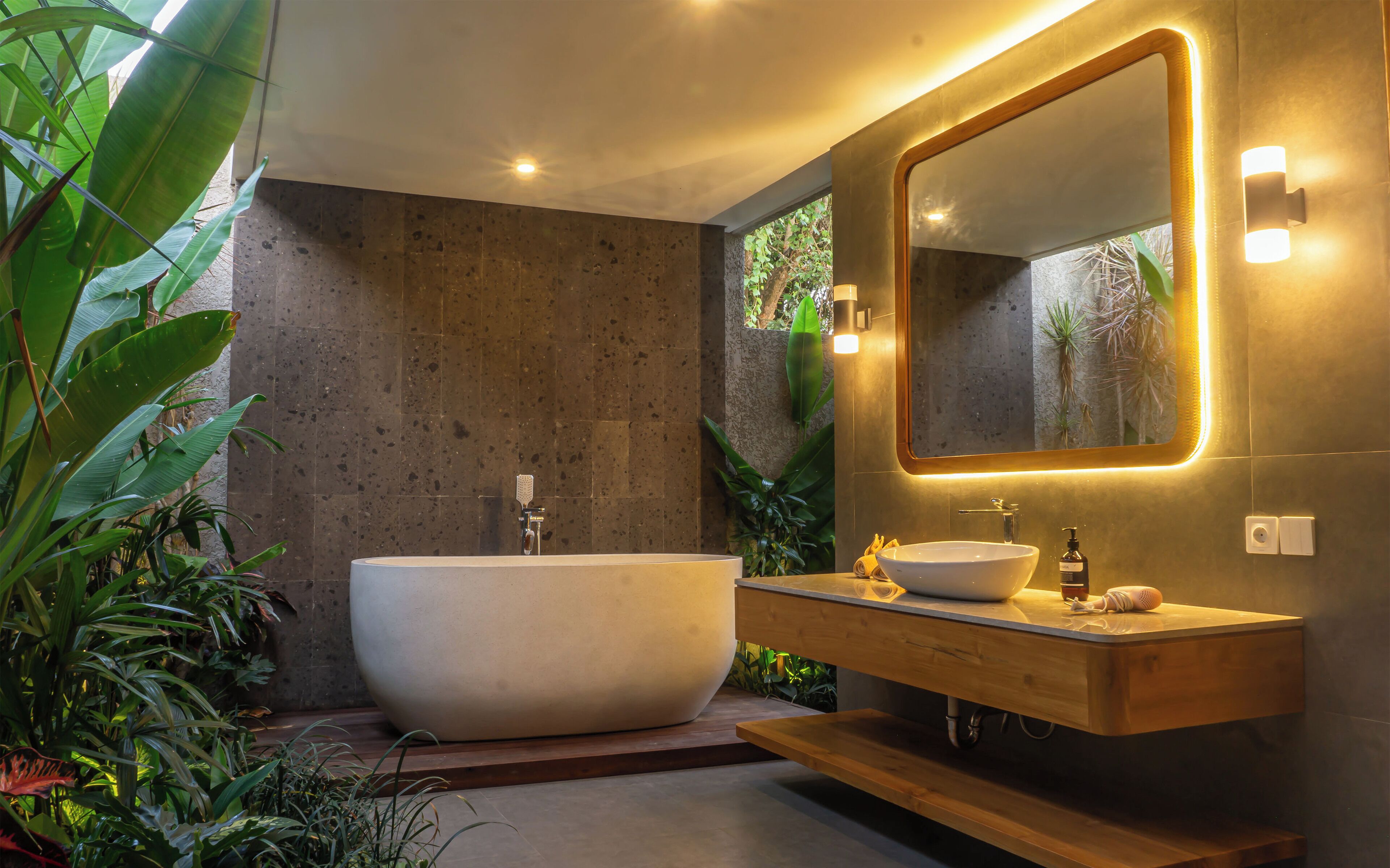 A modern bathroom with a freestanding bathtub, a wooden vanity, and a large mirror with integrated lighting.