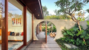 A wooden pathway leading to a seating area with a view of a garden and a pool. - Villa Suarga Des Anicca (Ubud)