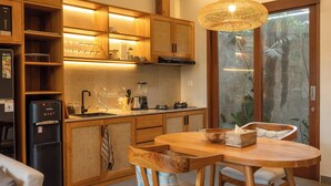 A modern kitchen with wooden cabinets, a built-in refrigerator, and a dining area with a wooden table and chairs. - Villa Suarga Des Anicca (Ubud)