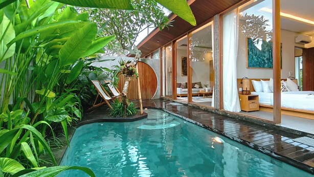 A modern pool area with a wooden deck, surrounded by lush greenery. - Villa Suarga Des Anicca (Ubud)