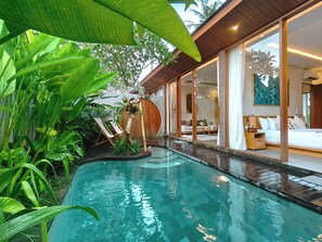 A modern pool area with a wooden deck, surrounded by lush greenery. - Villa Suarga Des Anicca (Ubud)