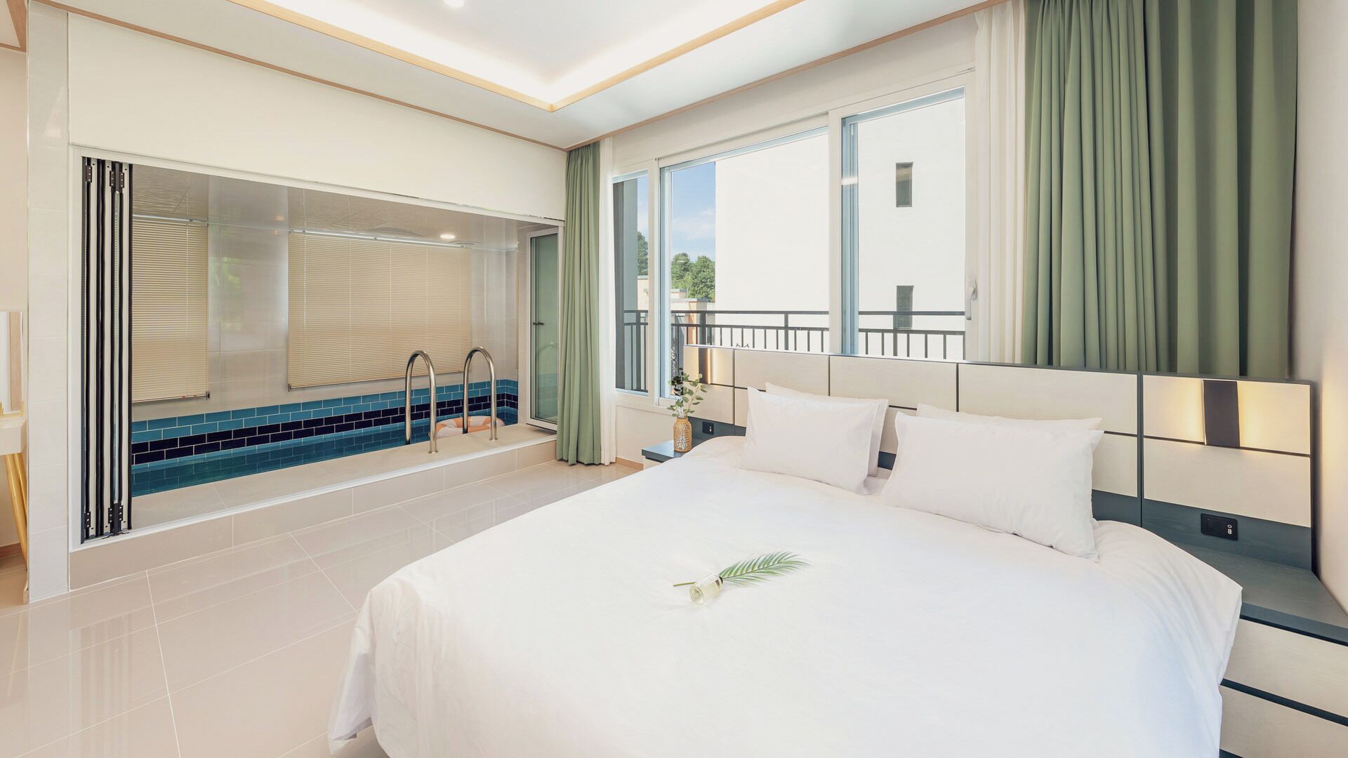 A hotel room with a large bed, a bathroom with a bathtub, and a balcony with curtains.