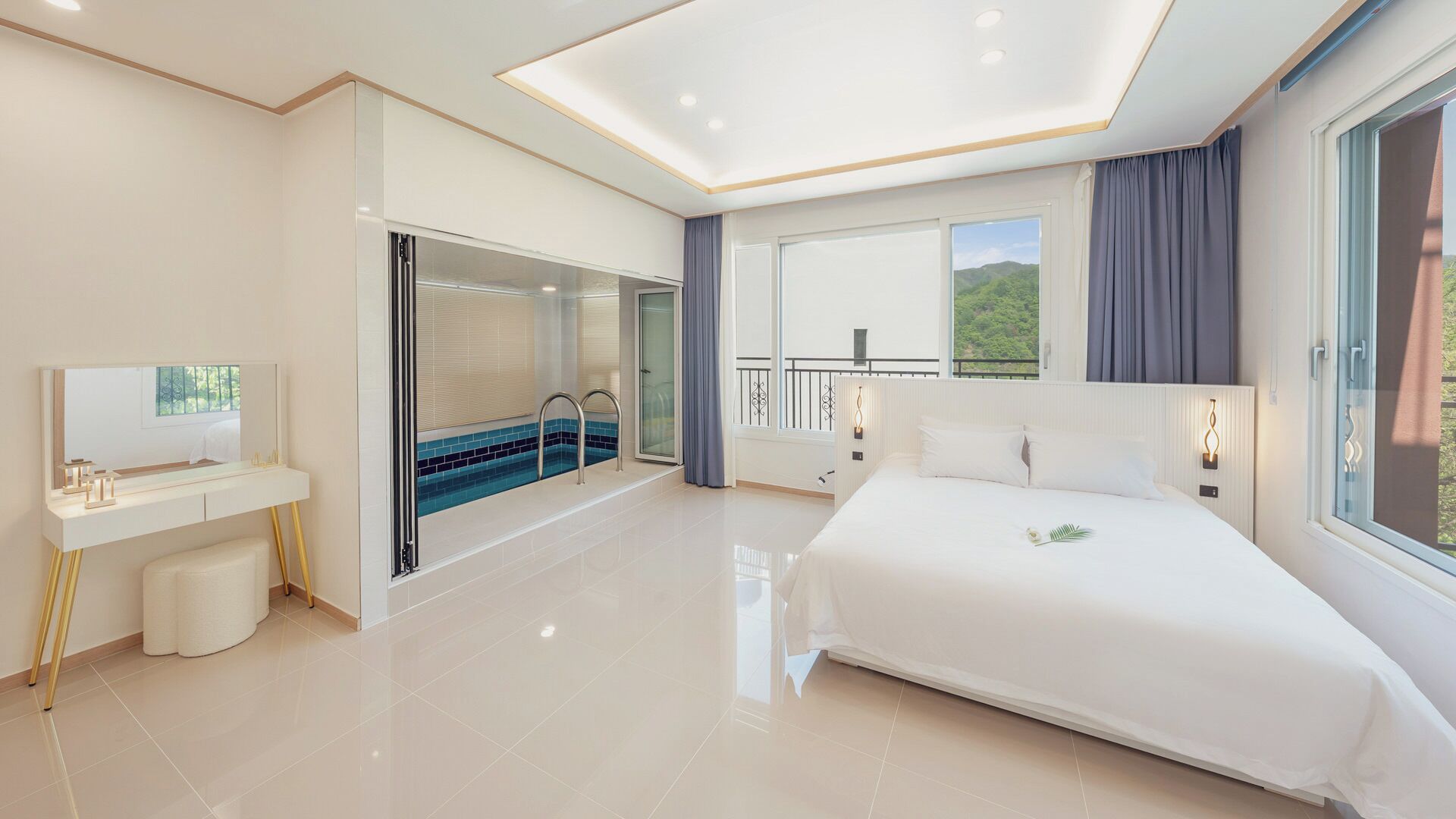 A modern hotel room with a large bed, a bathroom with a glass shower, a balcony with a view, and a desk with a mirror.