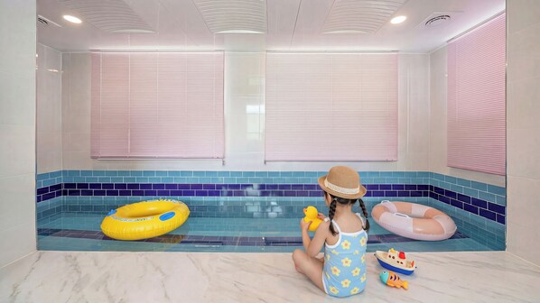 A child in a pool with inflatable rings, a toy boat, and a fish.