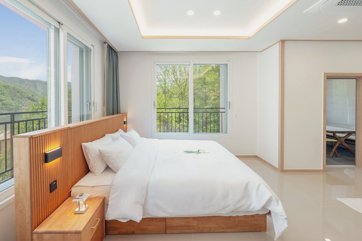 A bedroom with a bed, bedside table, and a view of a balcony.