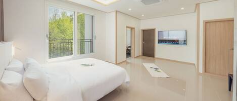 A modern hotel room with a large bed, a TV on the wall, and a balcony with a view of trees.