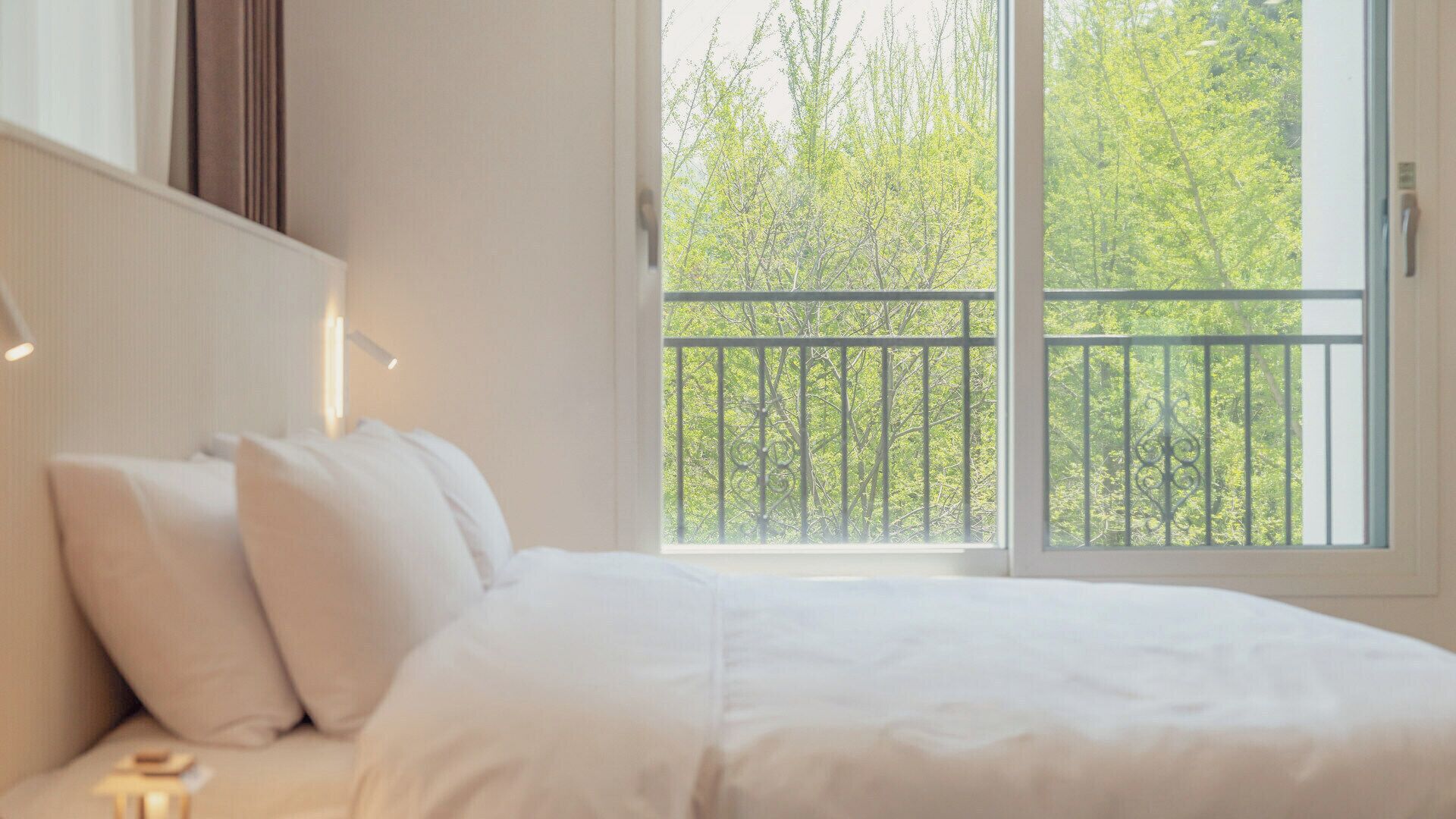 Une chambre avec une grande fenêtre, un lit et une table de chevet.