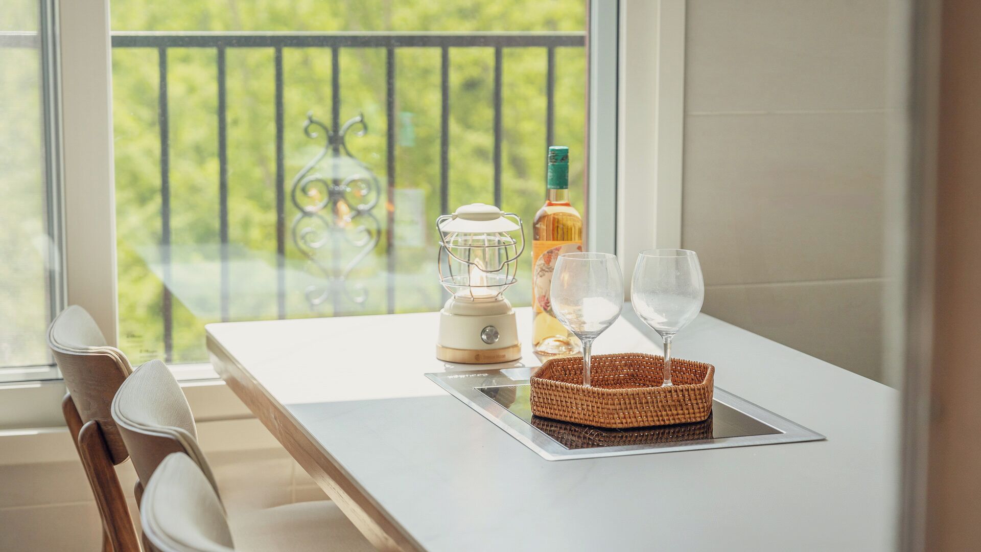 A balcony with a table, a table lamp, a bottle, and two glasses.