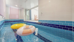 Una piscina interior con paredes de azulejos azules y dos flotadores inflables.