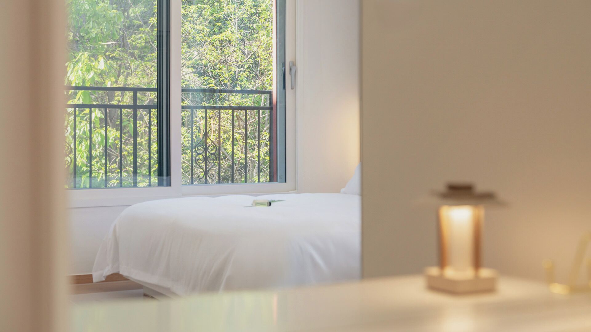 A bedroom with a bed, a window with a view of trees, and a bedside table with a lamp.