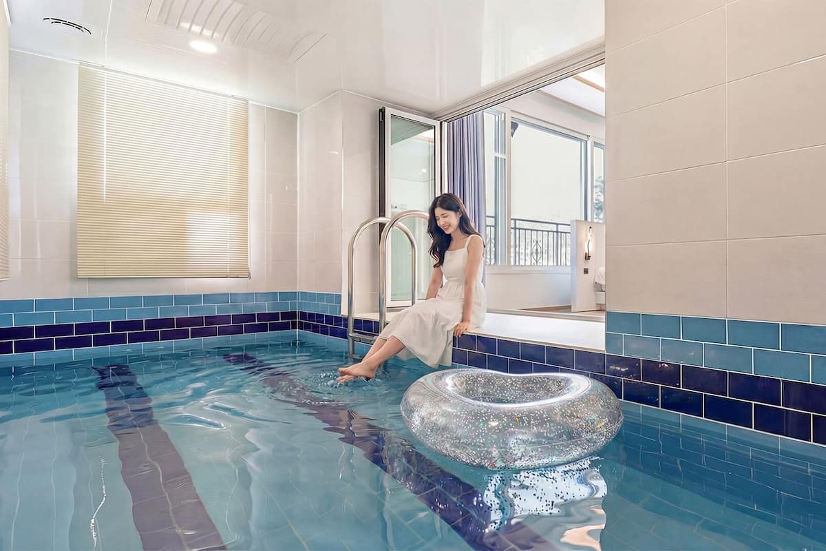 A woman in a white dress sitting by a pool with a heart-shaped float.