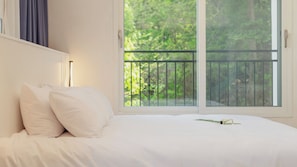 Un dormitorio con un amplio ventanal, una cama con ropa blanca y vistas a zonas verdes.