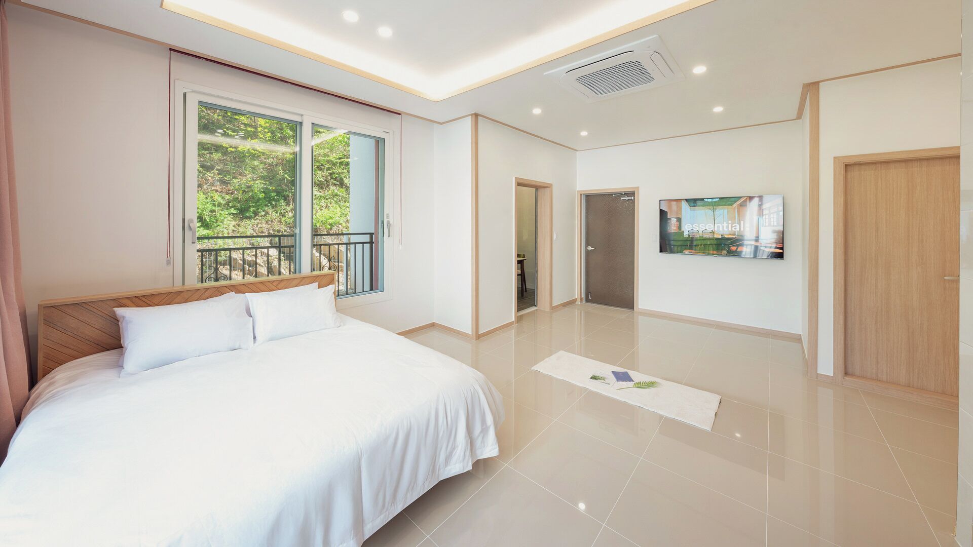 A modern hotel room with a large bed, a balcony, a television, and a door leading to another room.
