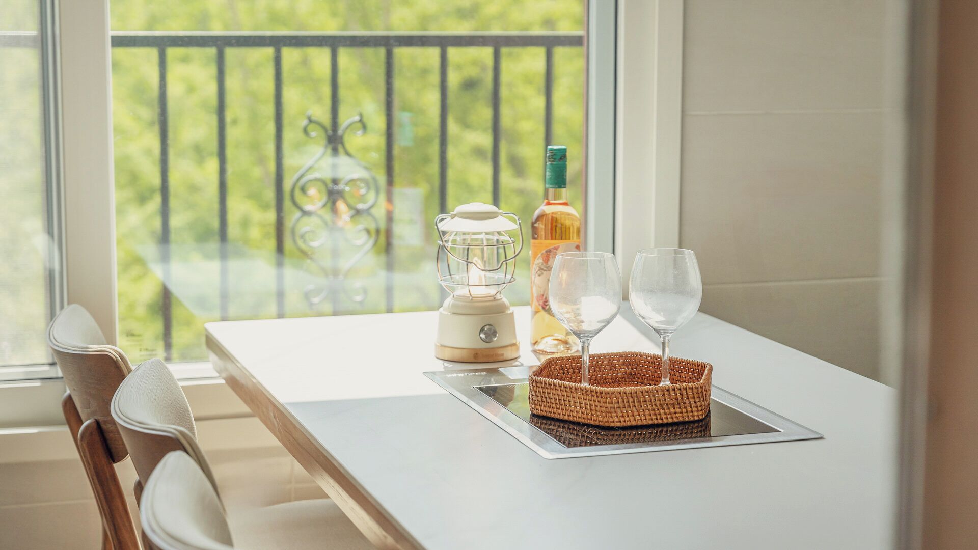 Un balcon avec une table, une bouteille, une carafe en verre et deux verres à vin, le tout disposé sur un plateau.
