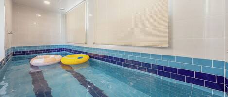 Una piscina interior con dos flotadores inflables, paredes de azulejos y una rejilla en el techo.