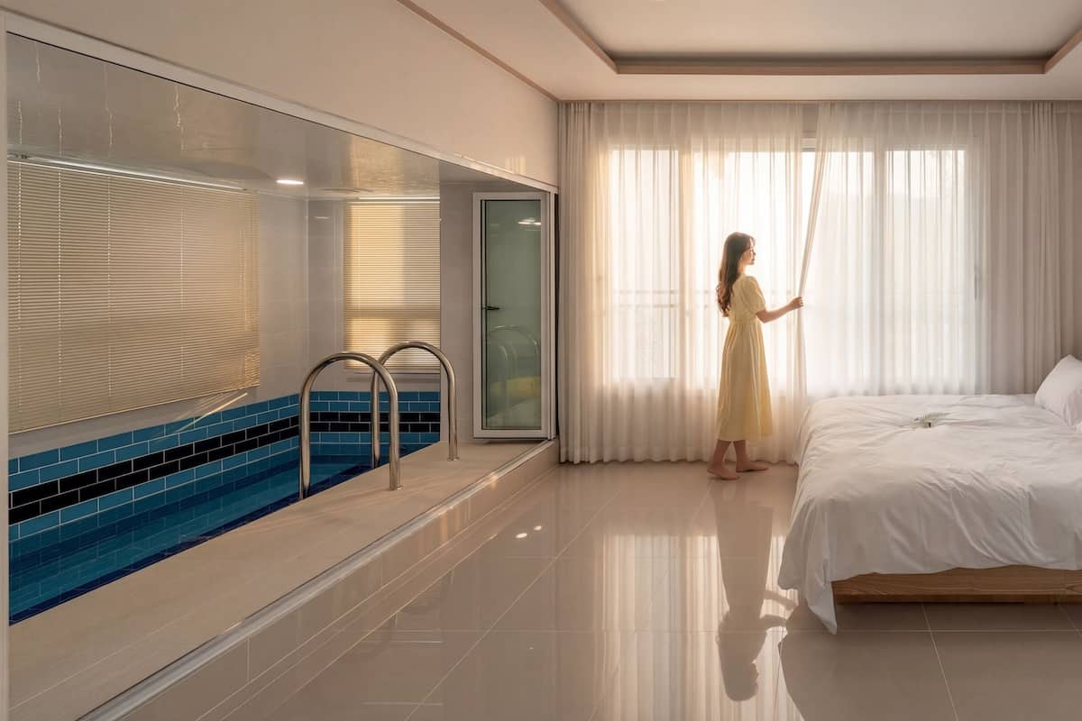 A modern hotel room with a large bed, a glass shower enclosure, and a small pool area.