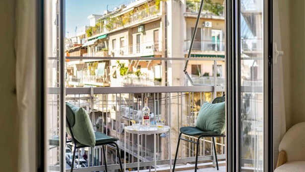 A balcony with two chairs, a small table, and a bottle of liquor.