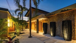 Une maison moderne avec une façade en pierre, une entrée bien éclairée et un chemin de gravier menant à la porte.
