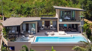 Une maison moderne à deux étages dotée d’une piscine, d’un espace extérieur aménagé et d’une végétation luxuriante.