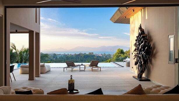 Un salon moderne doté d’une grande fenêtre donnant sur une piscine et des montagnes. On y trouve deux fauteuils confortables et une table basse agrémentée d’un vase décoratif.