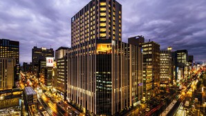 A high-rise building with multiple floors, surrounded by a busy urban street with visible traffic and illuminated signs. - THE GATE HOTEL SAPPORO by HULIC (Sapporo)