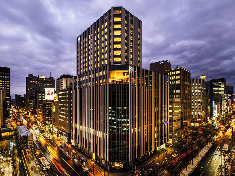 A high-rise building with multiple floors, surrounded by a busy urban street with visible traffic and illuminated signs.
