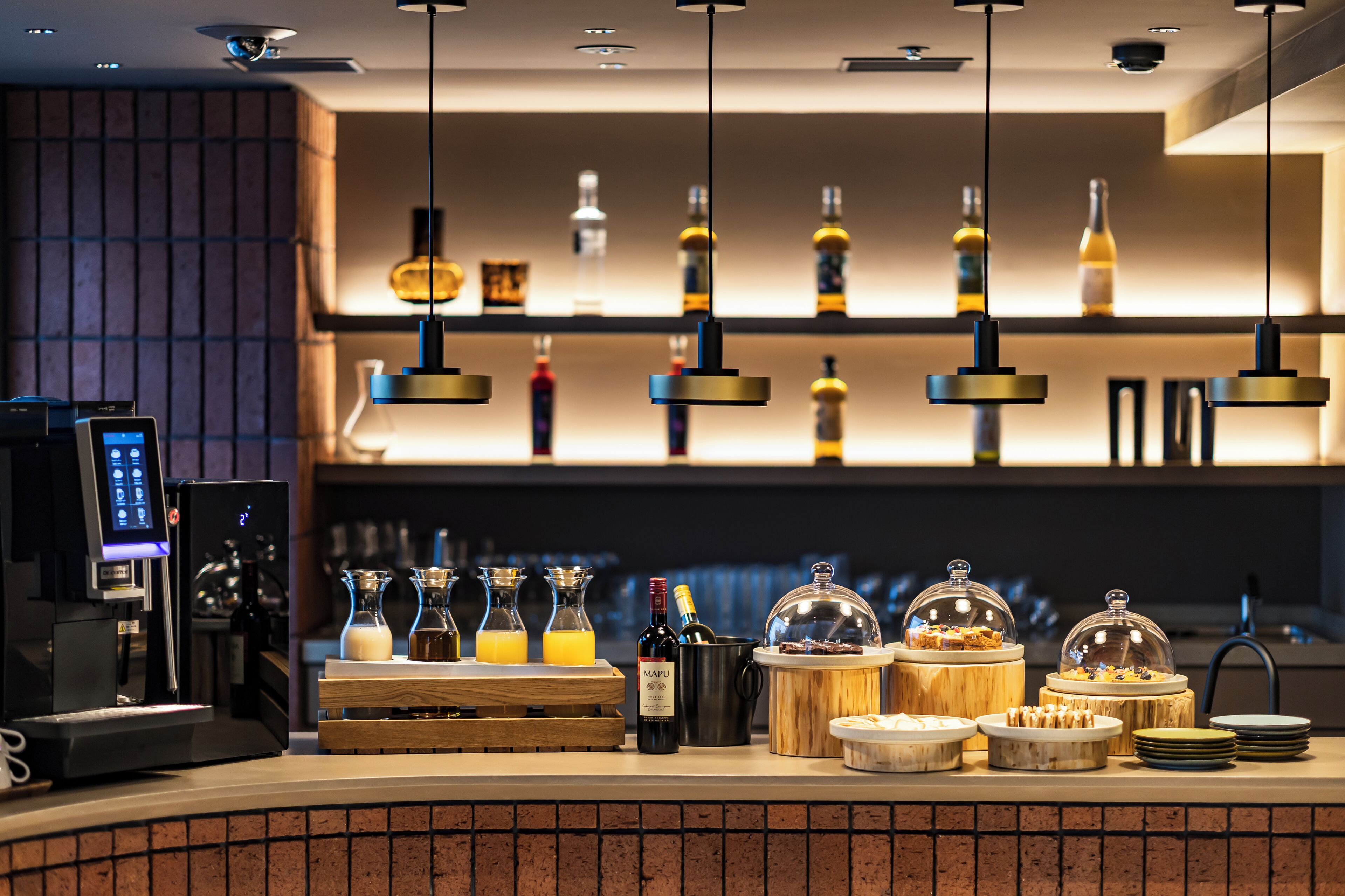 Zona de bar con una máquina de café, botellas de vino y diferentes alimentos.