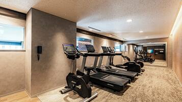 Un gimnasio moderno con cintas de correr, elípticas y una banca de pesas.