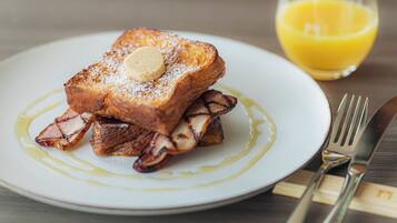 A plate of French toast with syrup and a butter pat, accompanied by a glass of orange juice.
