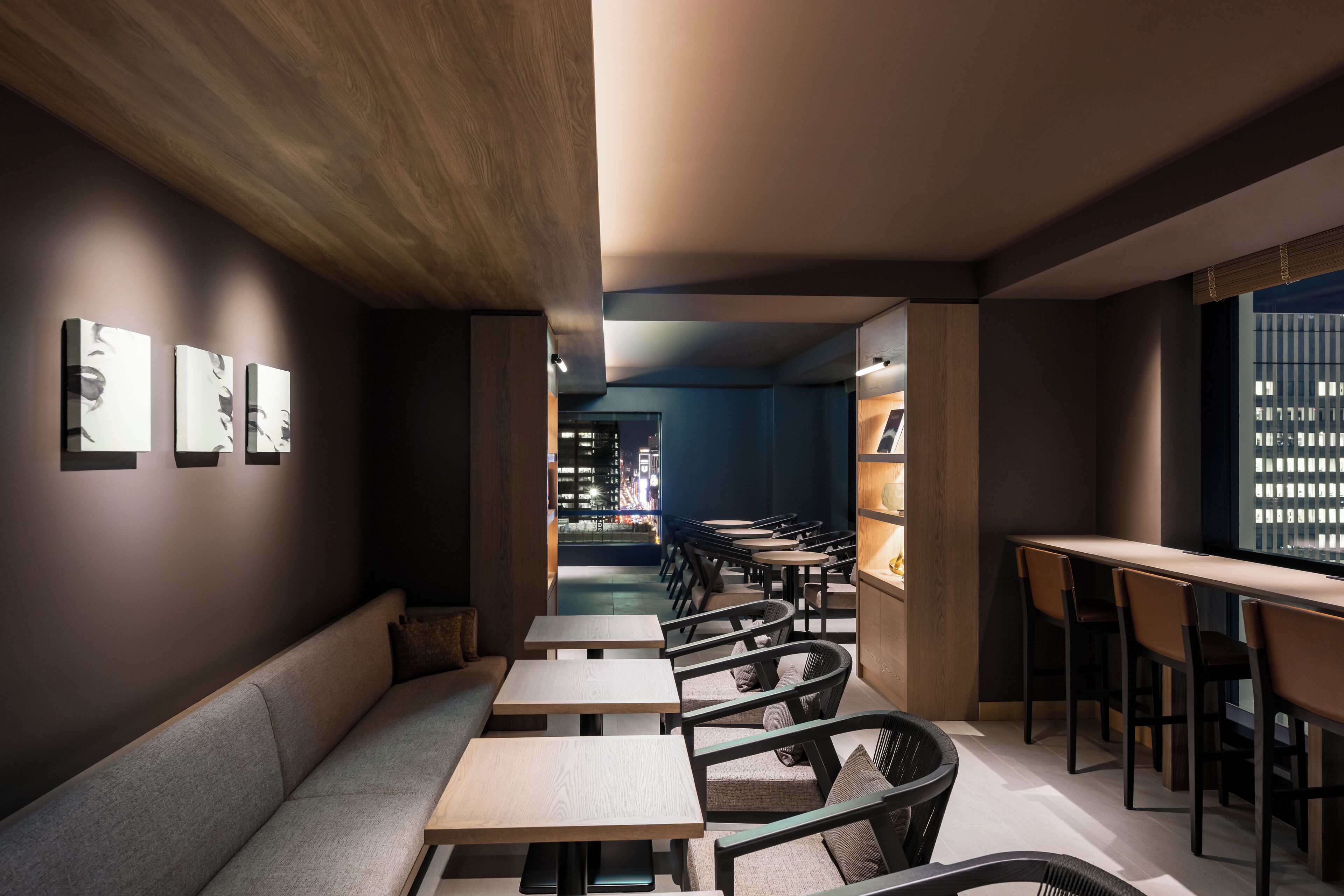 A modern interior with a long bench, multiple tables, and chairs arranged for dining.