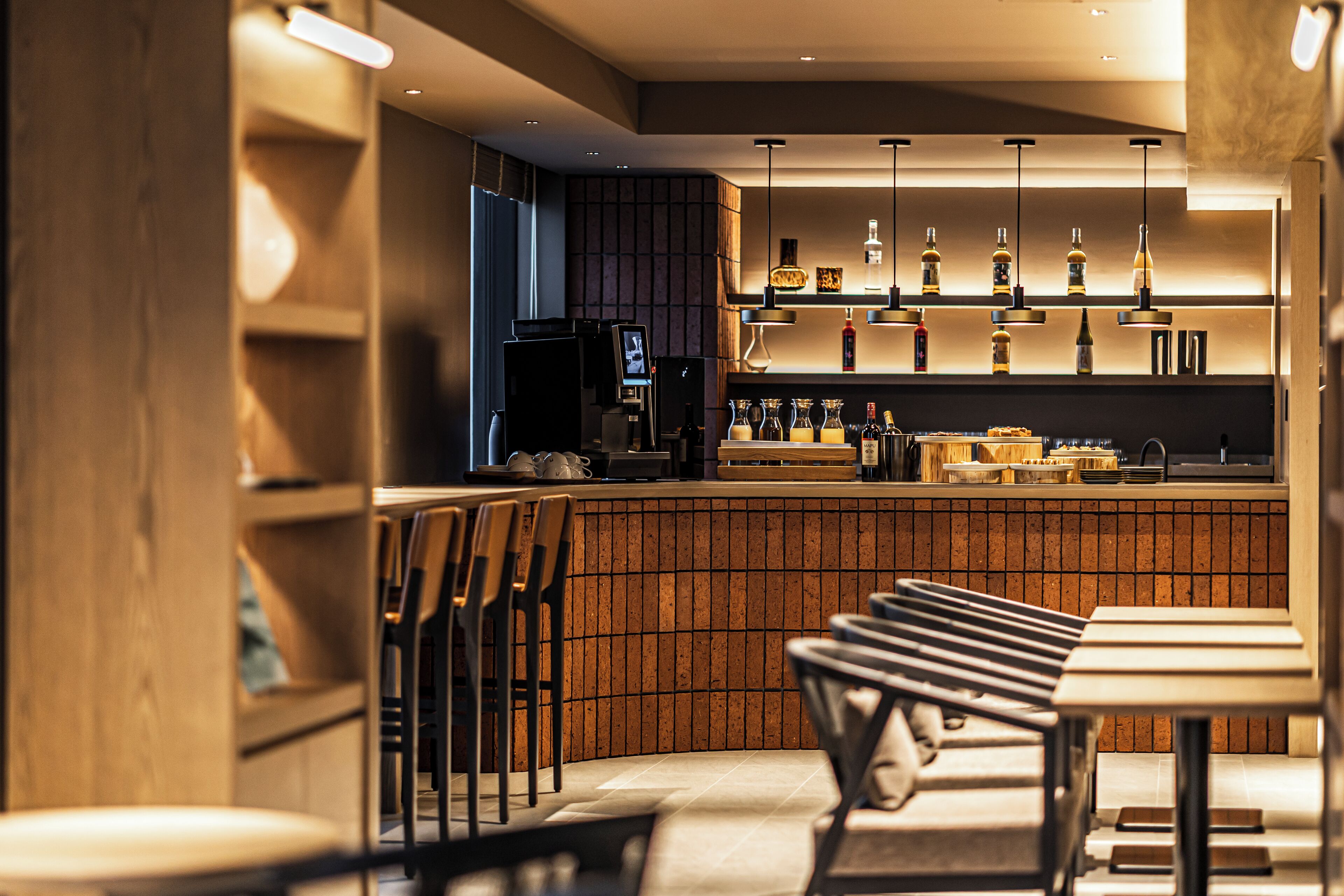 Een moderne bar met een houten toonbank, barkrukken en hangende hanglampen.