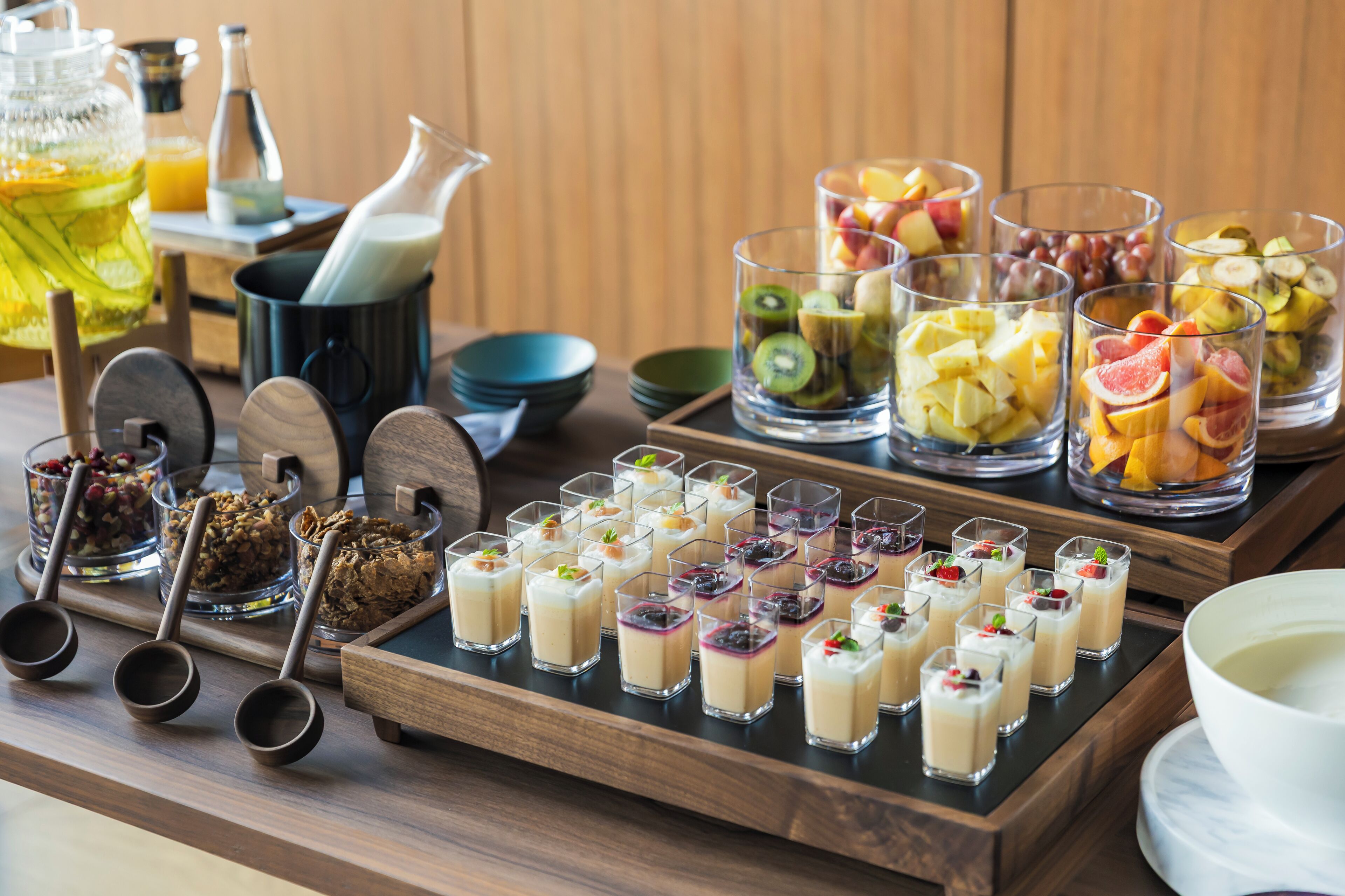 A breakfast buffet with various fruit options, granola, and small dessert cups.