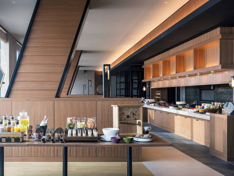 A modern kitchen with wooden cabinetry, a central island with various kitchen items, and a large window providing natural light.