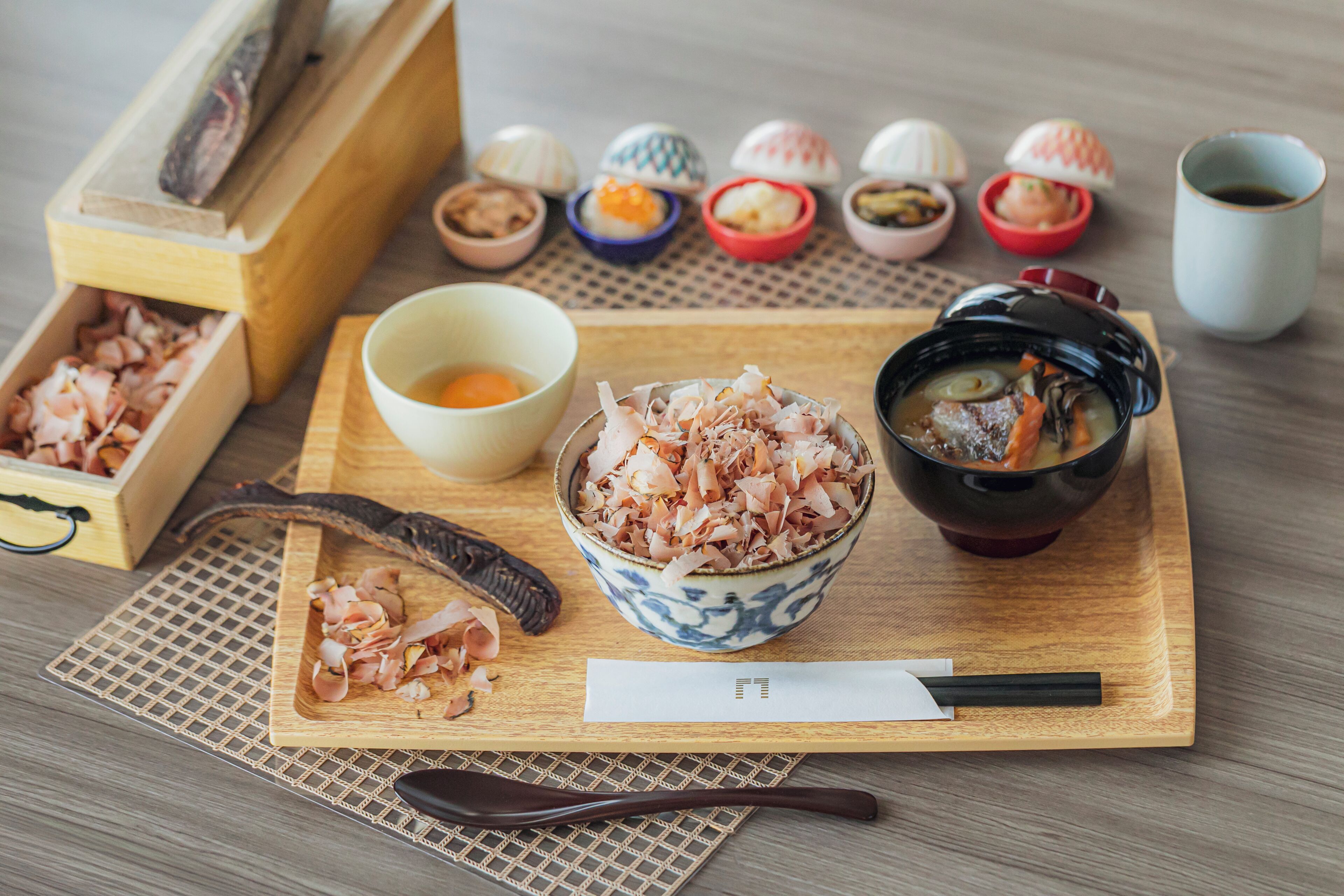 A wooden tray with various Japanese dishes, including a bowl of soup and several small bento boxes.