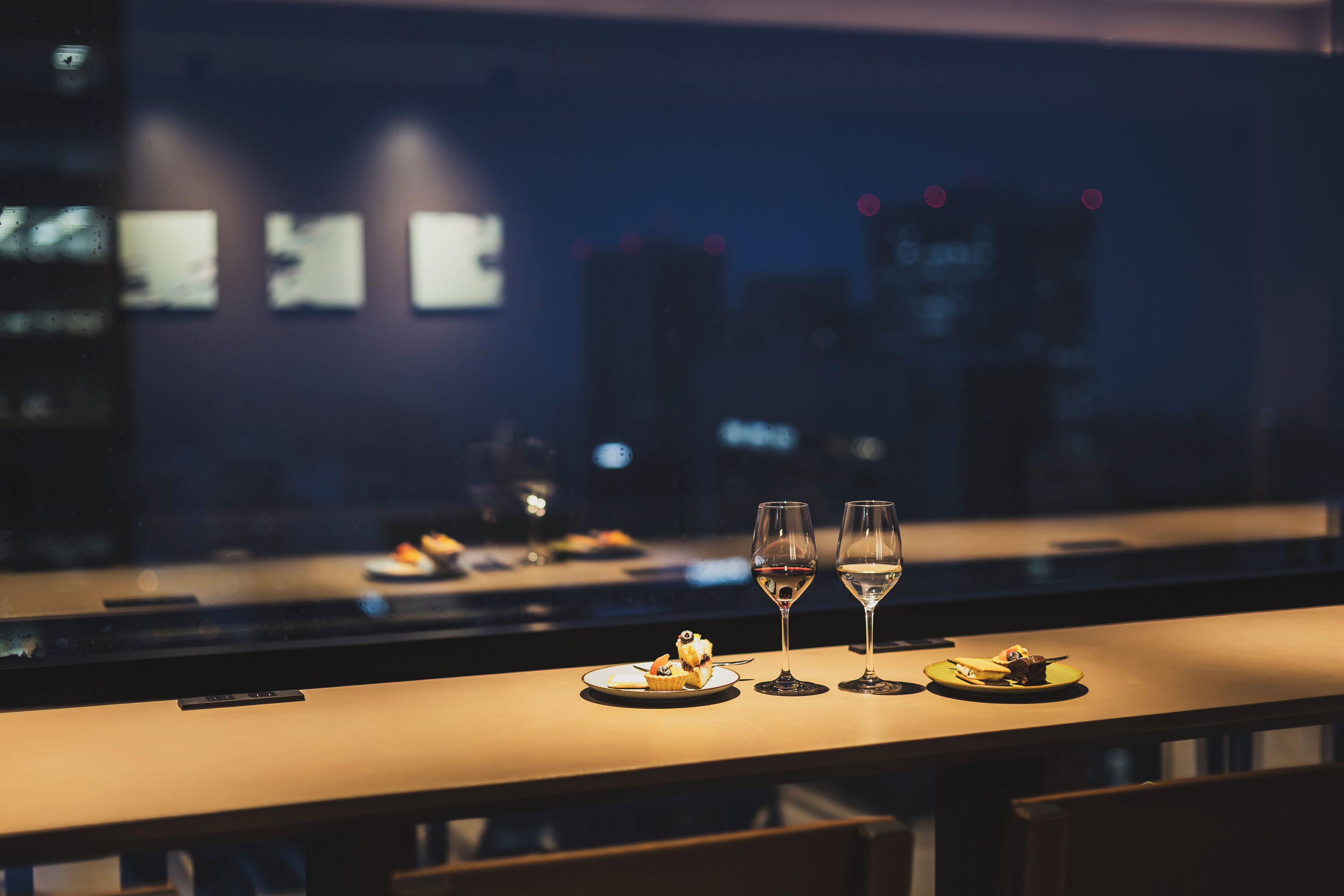 A dimly lit bar area with a table set for two, featuring a dessert and two glasses of wine.