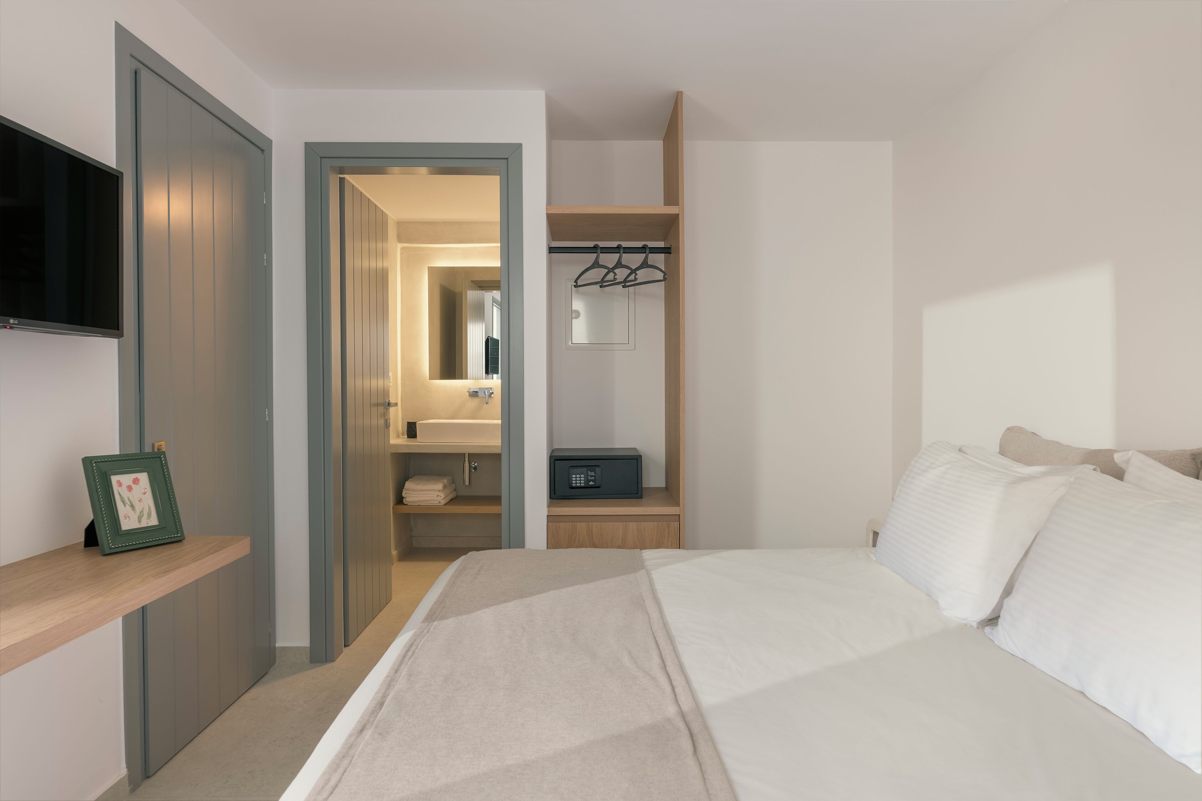 Un dormitorio con cama, televisor, armario y baño visible a través de una puerta abierta.