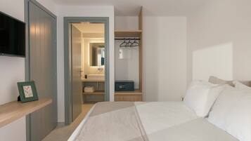 Un dormitorio con cama, televisor, armario y baño visible a través de una puerta abierta.