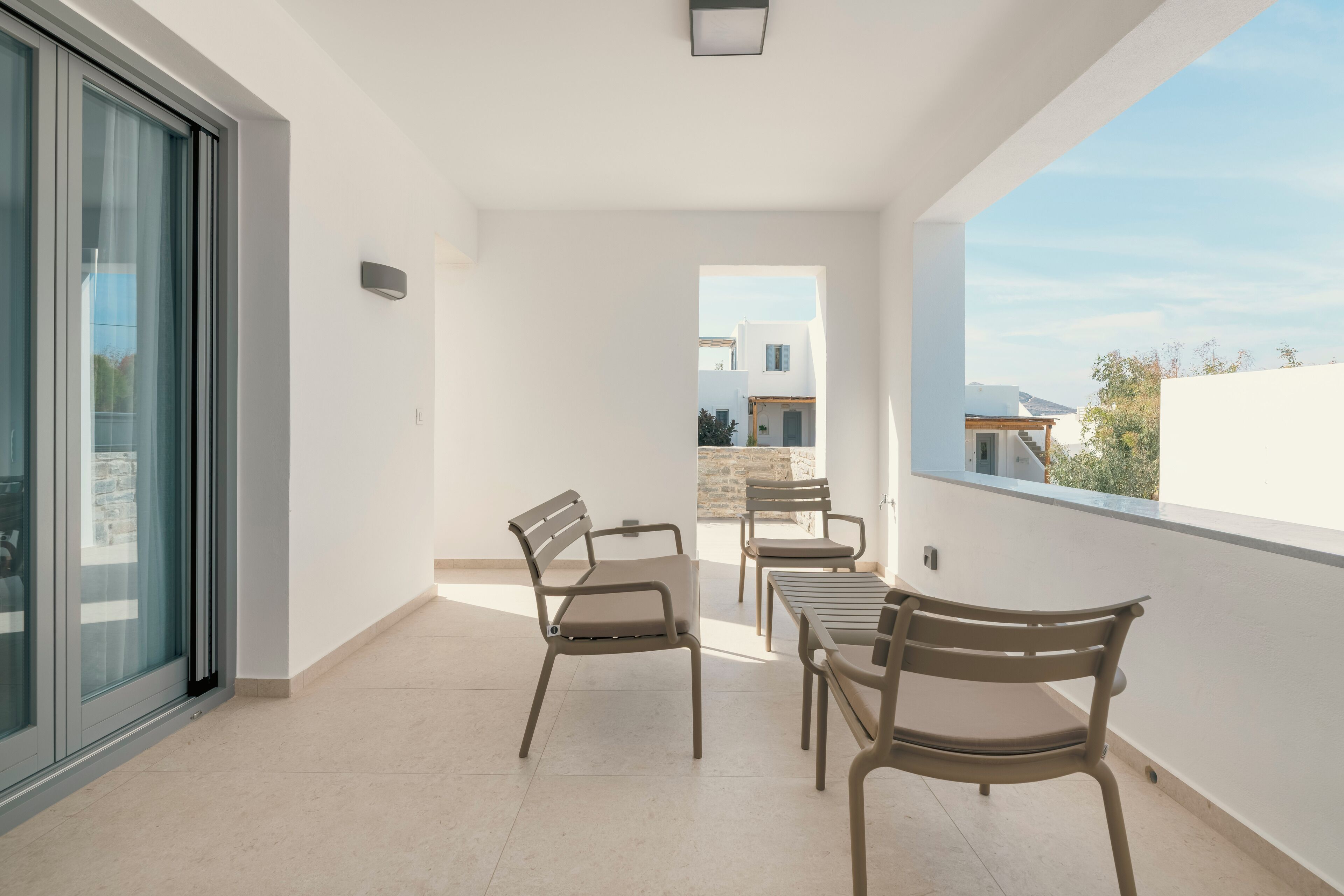Un balcon avec une table et des chaises, une porte-fenêtre coulissante et une vue sur les bâtiments au loin.