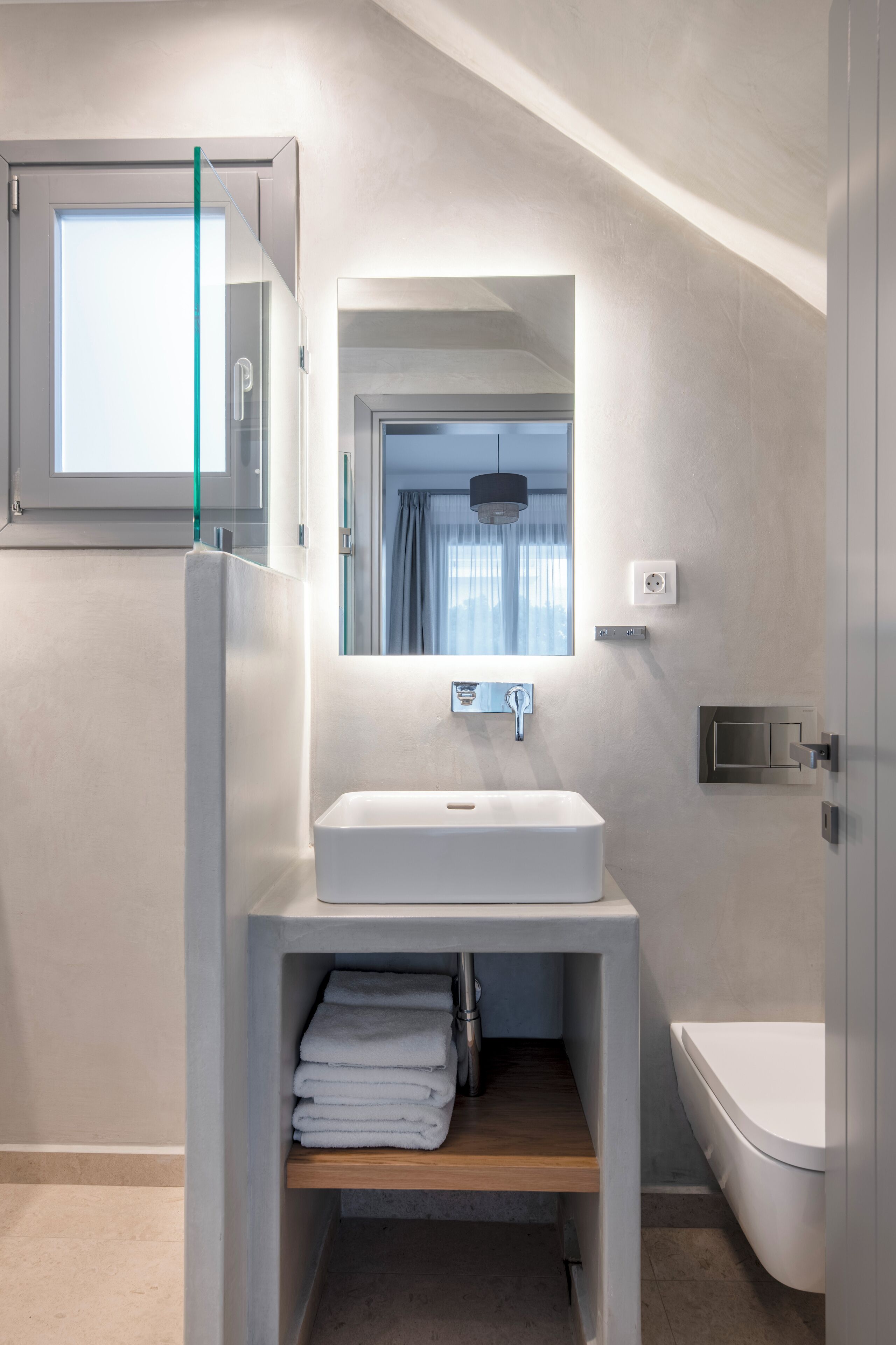 Un baño moderno con un lavamanos blanco, un espejo encima y un inodoro a la derecha.