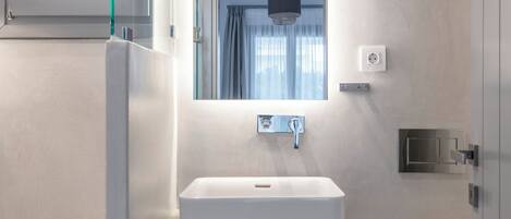 Un baño moderno con un lavamanos blanco, un espejo encima y un inodoro a la derecha.