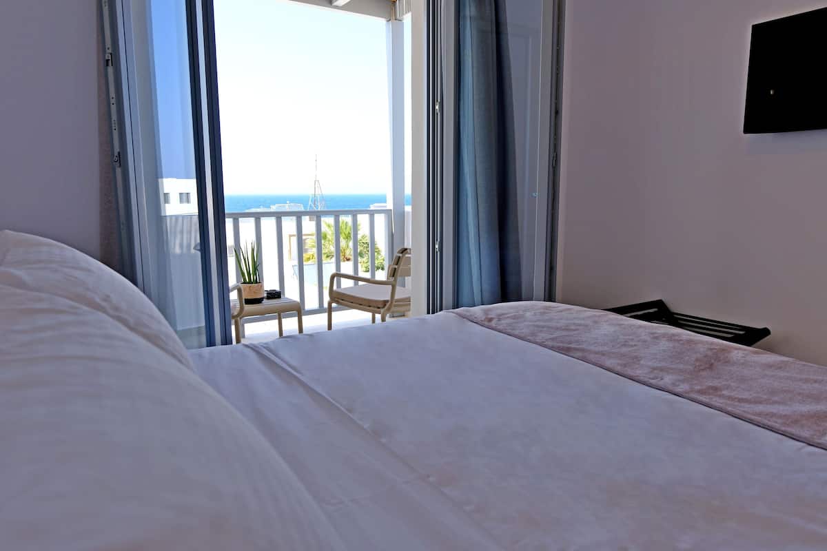 Un dormitorio con una cama grande, una silla y vistas al mar desde un balcón.