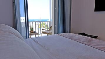 Un dormitorio con una cama grande, una silla y vistas al mar desde un balcón.