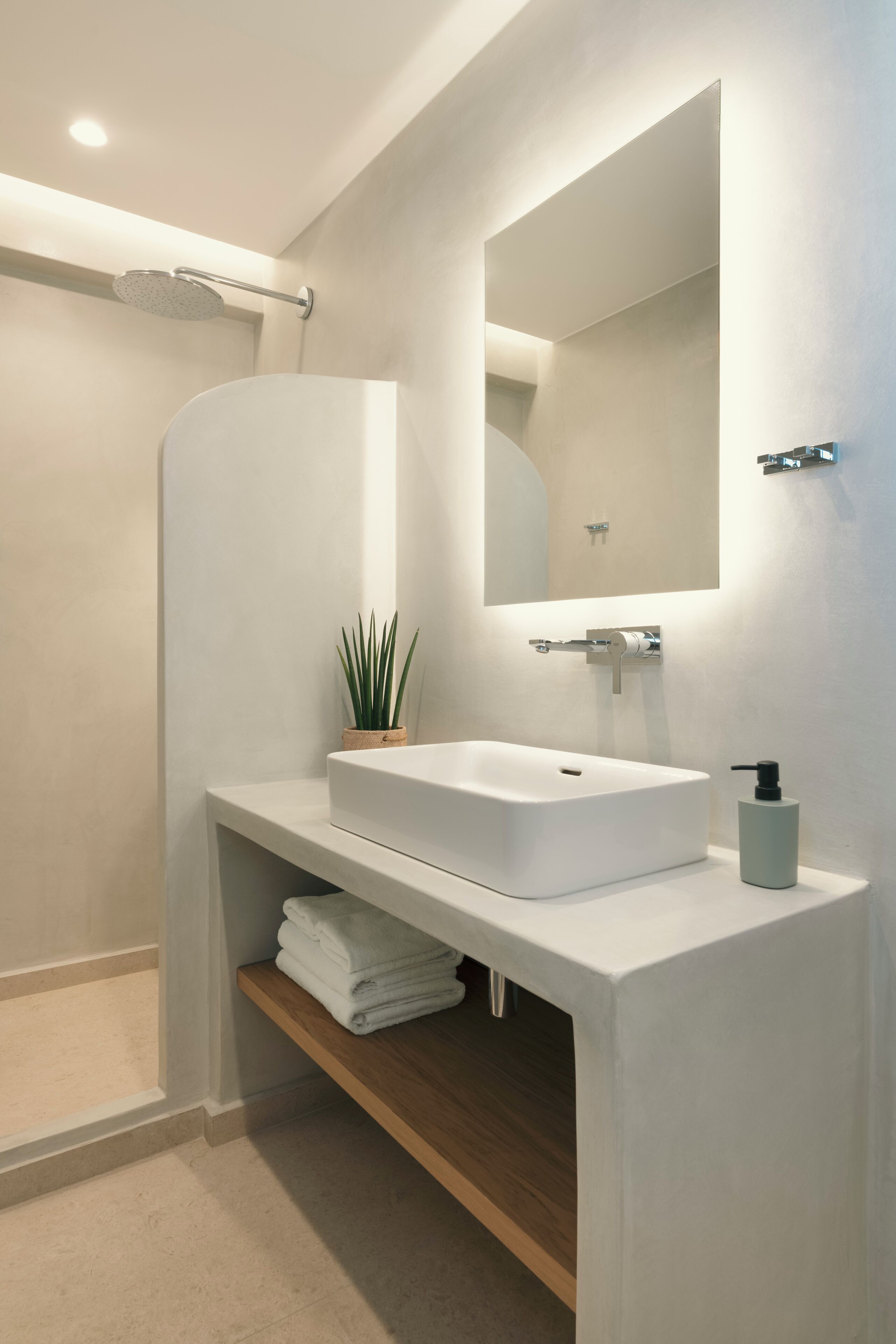 A modern bathroom with a white sink, a mirror, a shower, and a small potted plant.