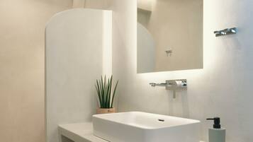 A modern bathroom with a white sink, a mirror, a shower, and a small potted plant.