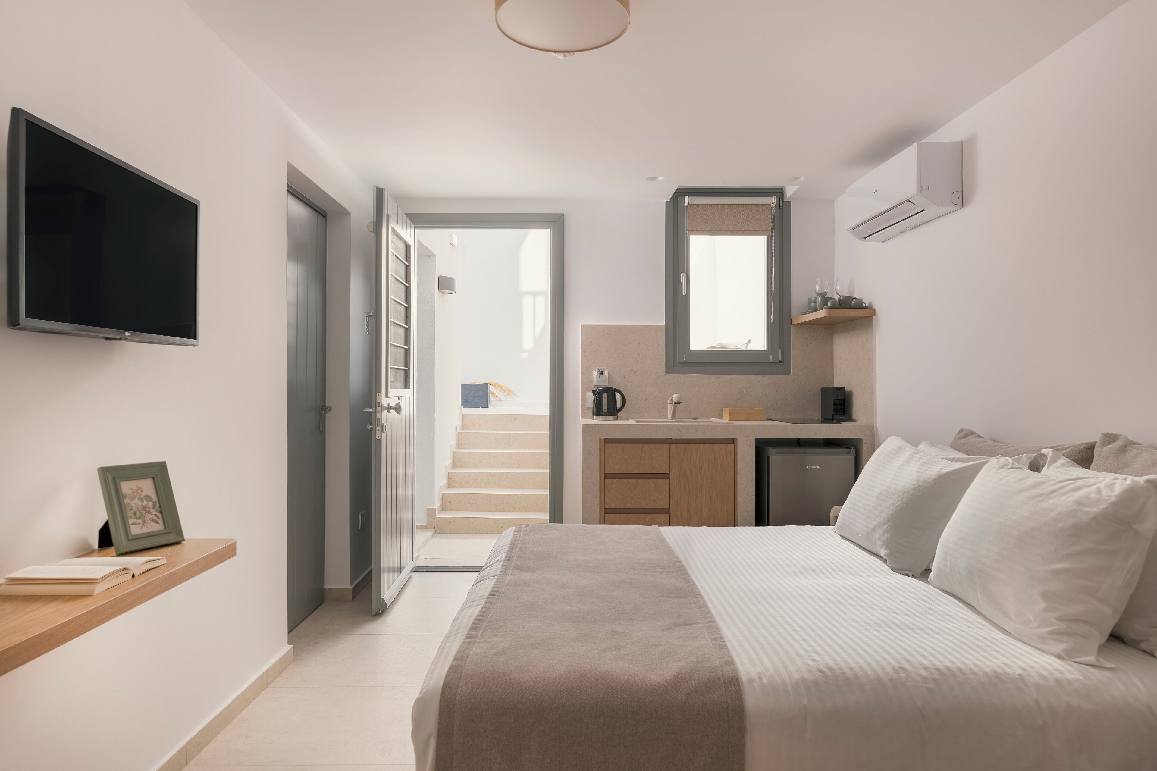 Un dormitorio moderno con cama, mesita de noche y televisor fijado a la pared.