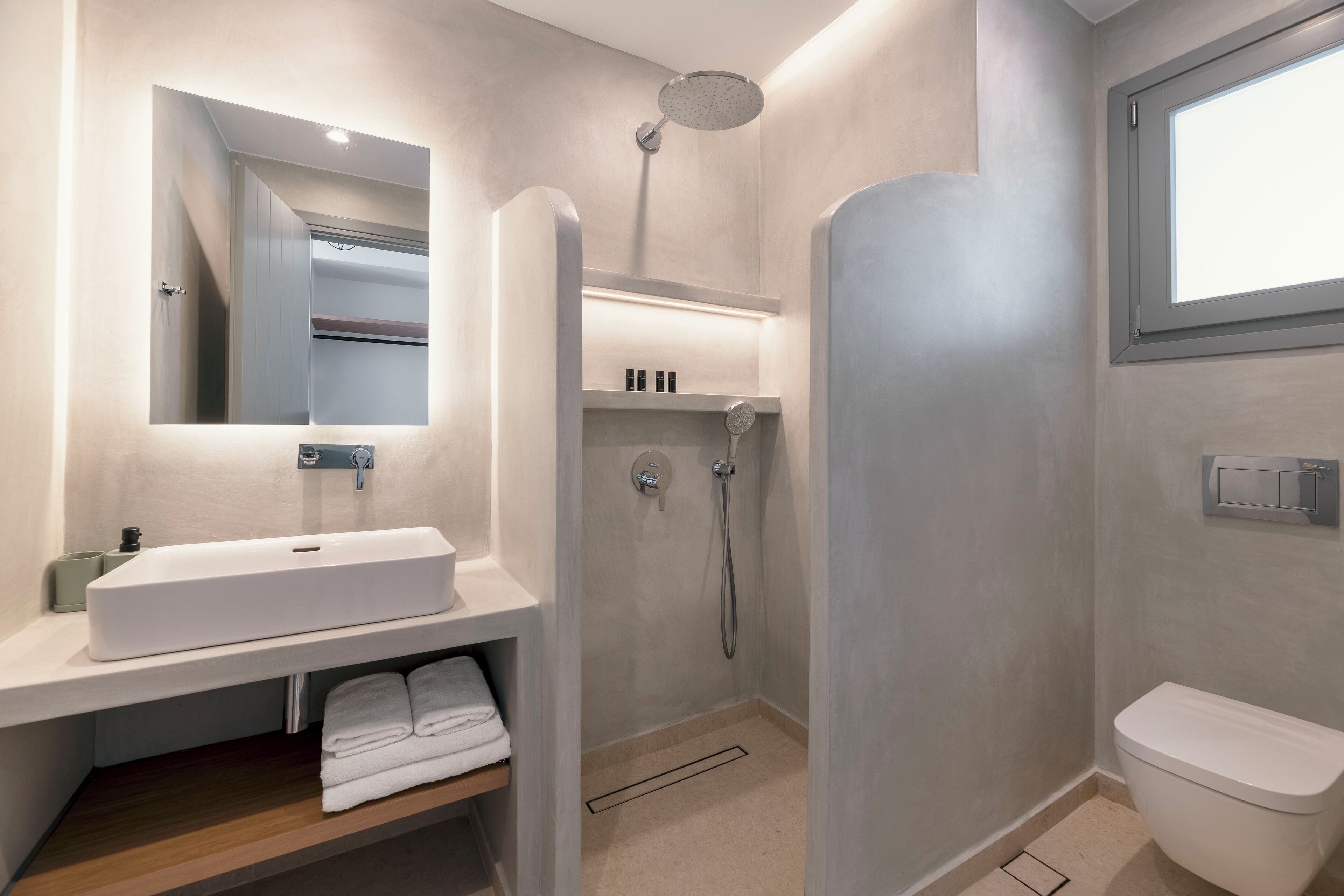 Une salle de bain moderne avec un grand miroir, un lavabo blanc, une douche et des toilettes.