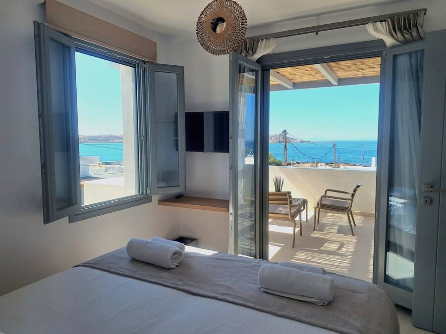 Un dormitorio con cama, dos ventanas, televisión y balcón con vista al mar.