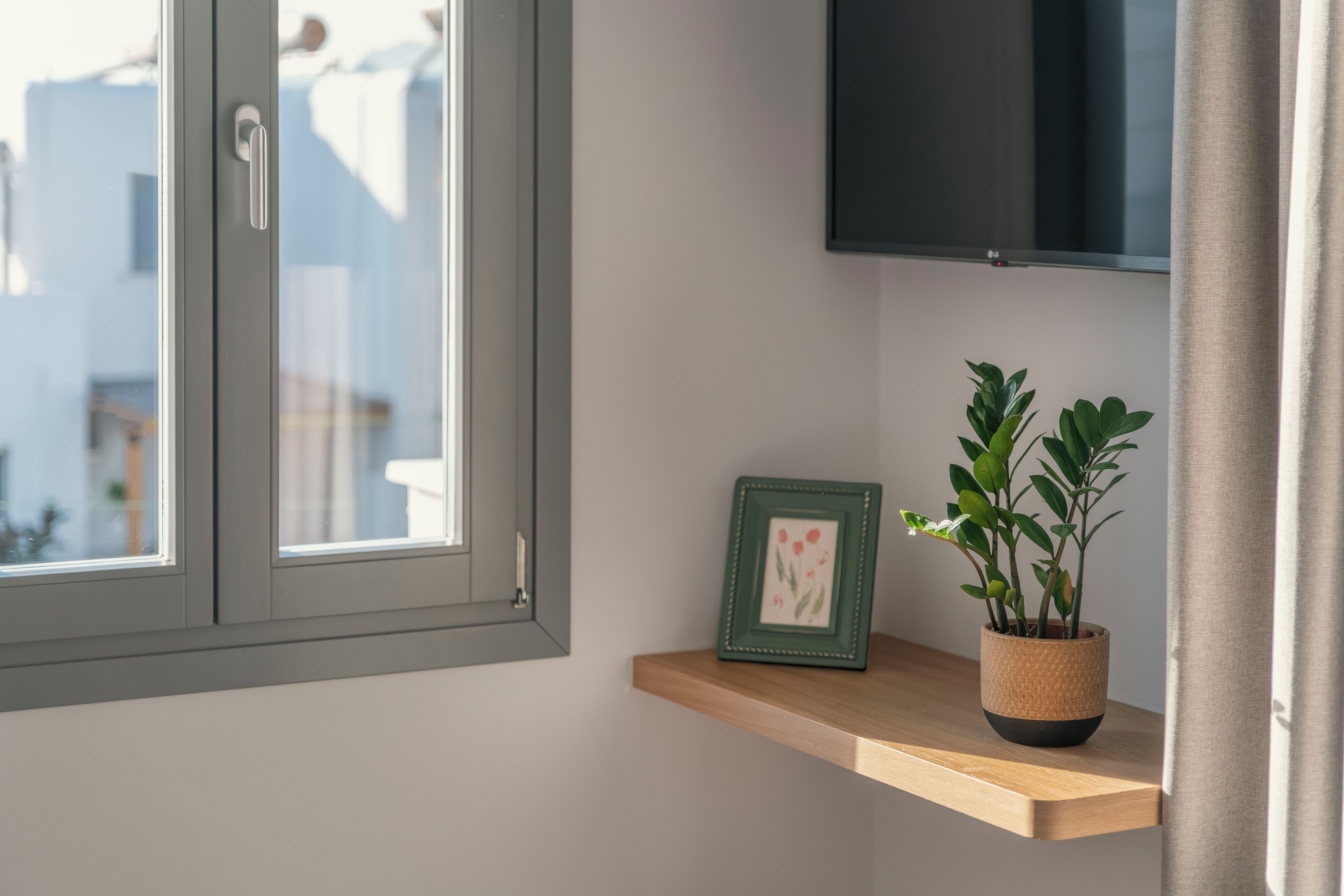 Una habitación con ventana, estante de madera, un cuadro enmarcado y una planta en maceta.