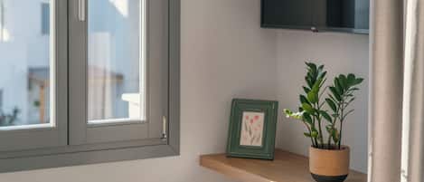 Een kamer met een raam, een houten plank, een lijst met een afbeelding en een potplant.